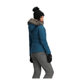 Obermeyer Women's Tuscany Elite Insulated Jacket - A woman wearing a blue jacket with a gray fur-lined hood, standing in front of a white background.