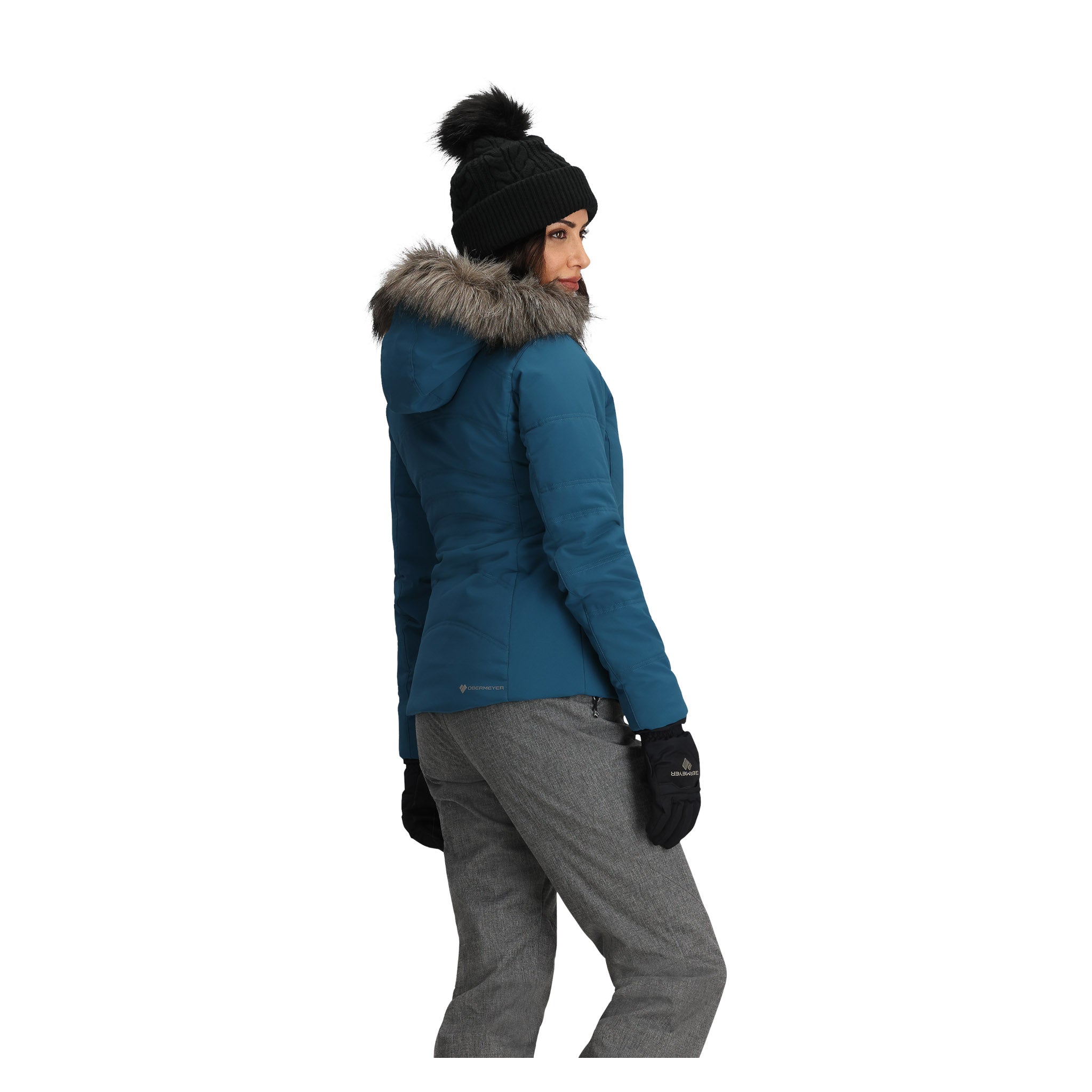 Obermeyer Women's Tuscany Elite Insulated Jacket - A woman wearing a blue jacket with a gray fur-lined hood, standing in front of a white background.