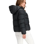 Obermeyer Women's Calypso Down Jacket 2025 - A black down jacket with a hood, worn by a woman with long brown hair and white pants.