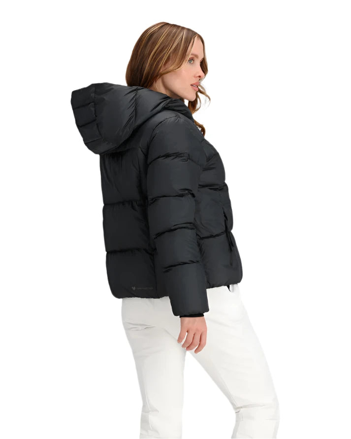 Obermeyer Women's Calypso Down Jacket 2025 - A black down jacket with a hood, worn by a woman with long brown hair and white pants.