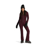 Obermeyer Women's Katze Insulated Suit 2025 - A burgundy insulated snowsuit with a zippered front and gold zipper pulls, worn by a model posing in front of a white background.