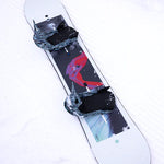 Burton Talent Scout Snowboard 2025 - A black snowboard with a red and blue graphic of a person riding on it, lying in the snow.