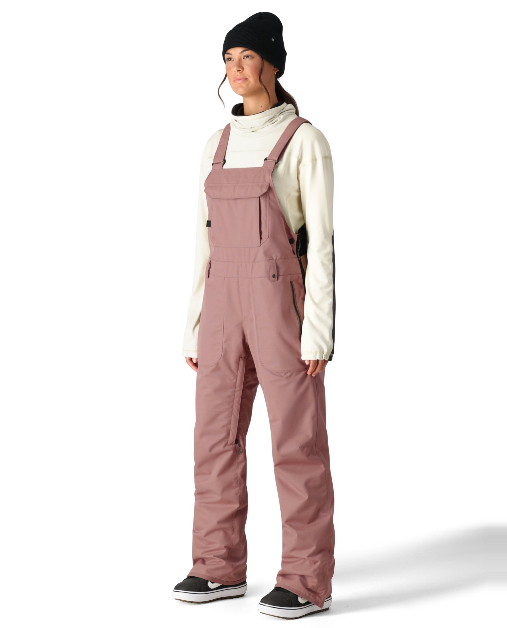 The 686 Black Magic Insulated Bib Pants are showcased from the side view, highlighting their black color and zippered pockets.