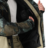 The 686 Geo Insulated Jacket 2025 has an olive green and brown camouflage pattern with tan accents on the trim.