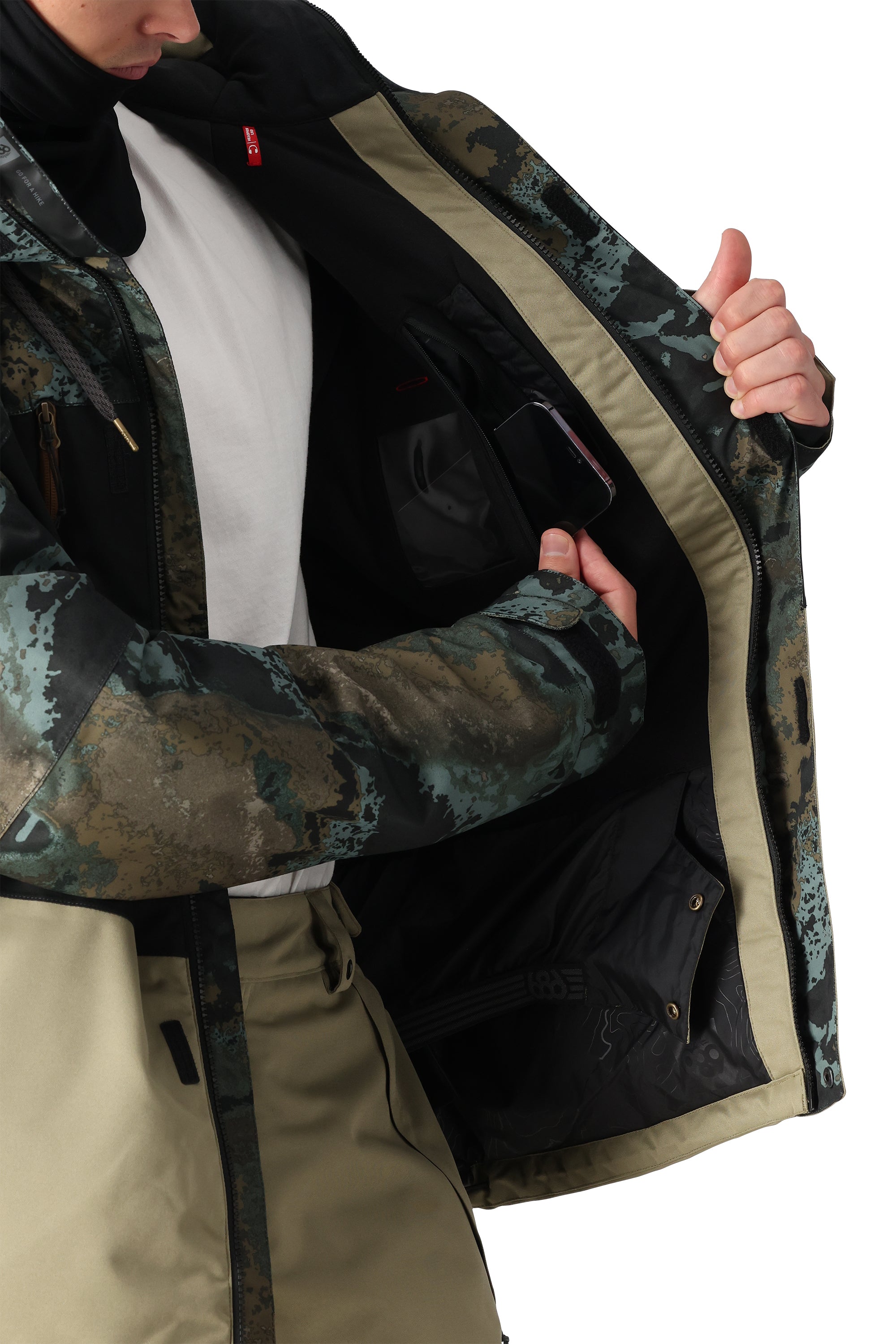 The 686 Geo Insulated Jacket 2025 has an olive green and brown camouflage pattern with tan accents on the trim.