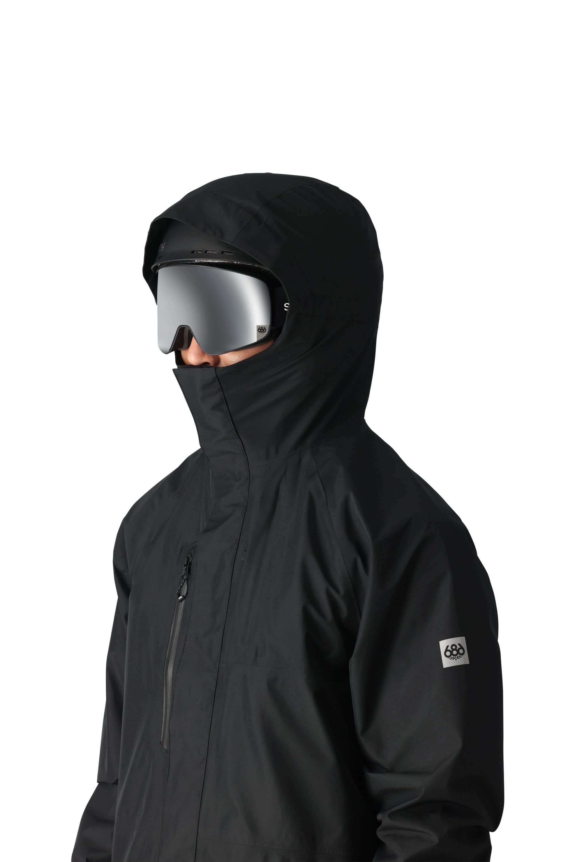 The 686 Gore-Tex Core Shell Jacket 2025 is black with a hood and a zipper that goes up to the chin.