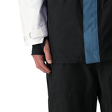 The 686 GORE-TEX Core Shell Jacket 2025 features a predominantly black design with light blue accents on the chest and shoulders.