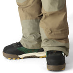 The 686 Men's GORE-TEX Stretch Dispatch Bib 2025 is depicted in khaki and tan, showcasing a side view with a zippered fly and adjustable leg straps.