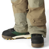 The 686 Men's GORE-TEX Stretch Dispatch Bib 2025 is depicted in khaki and tan, showcasing a side view with a zippered fly and adjustable leg straps.