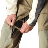 The 686 Men's GORE-TEX Stretch Dispatch Bib Pant in tan and khaki has multiple zippered pockets and adjustable Velcro straps on the side.