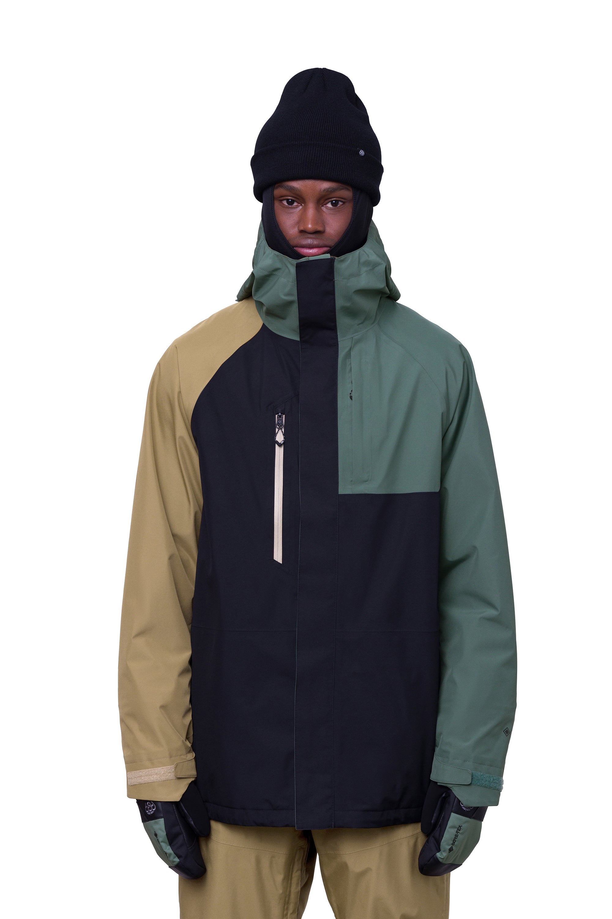 The 686 Gore-Tex Core Shell Jacket in black, tan, and green has a zippered front with two front pockets under a hood.