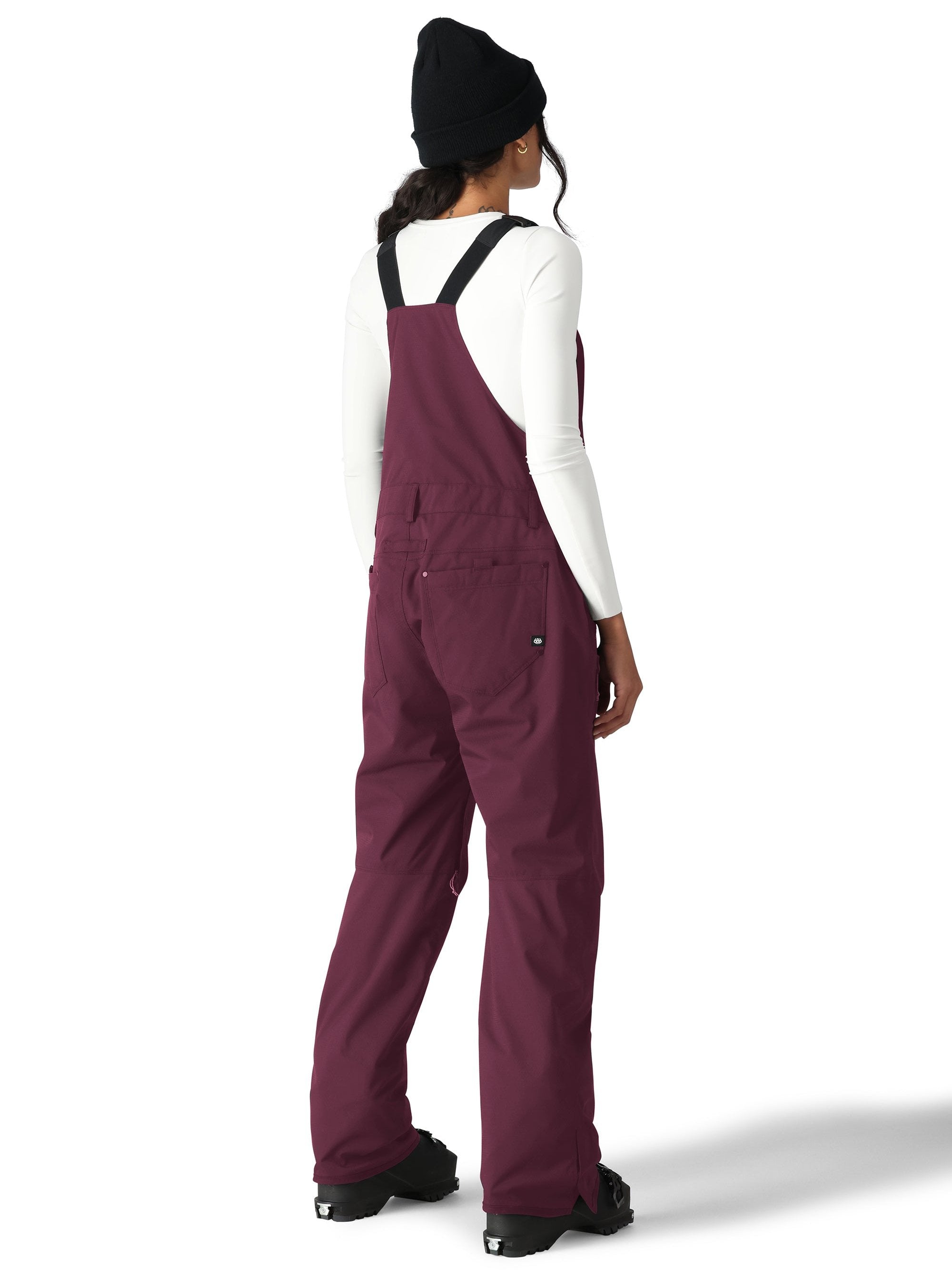 The 686 Women's Black Magic Insulated Bib features black suspenders and a bib leg with a visible zippered pocket on the side.