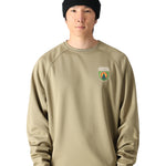 The 686 Men's Bonded Fleece Crew 2025 has a predominantly dark green color with lighter green accents and appears to be worn by someone standing in front of a snowy landscape.