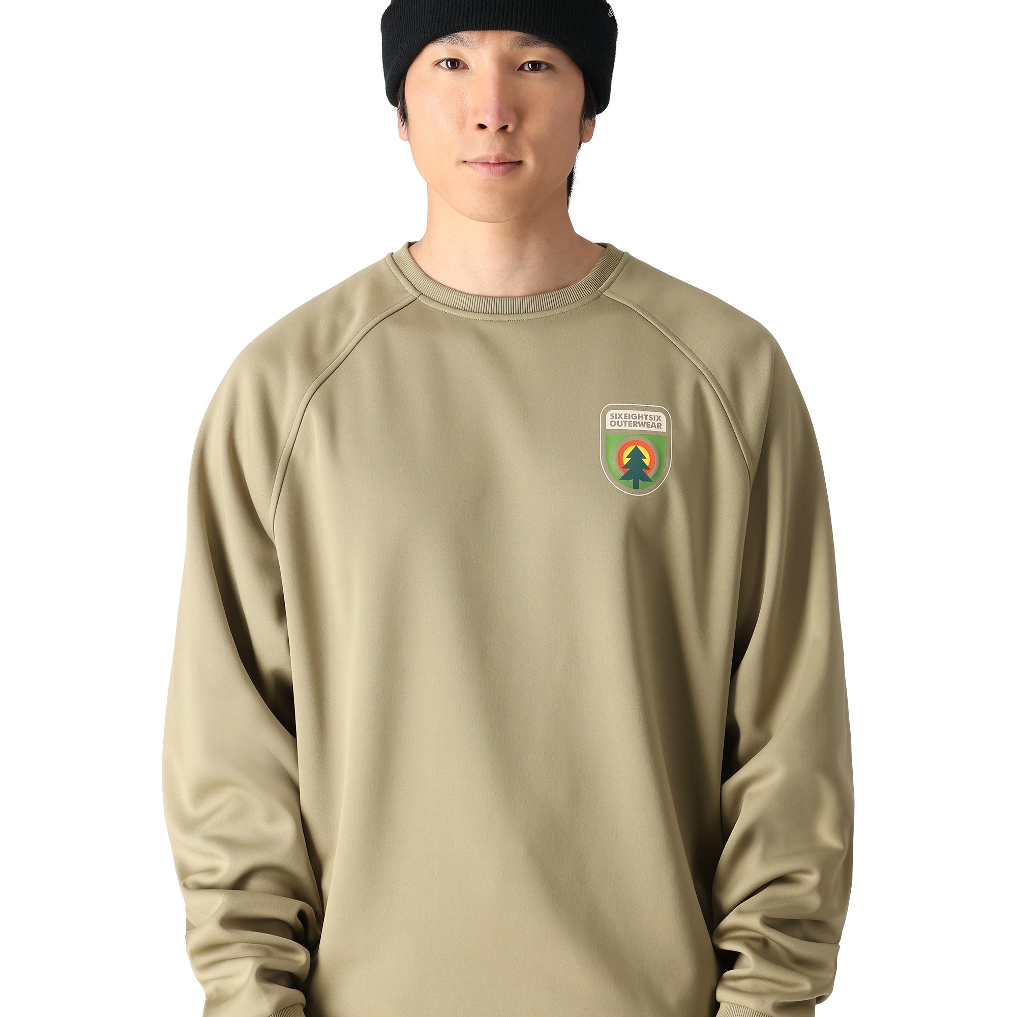 The 686 Men's Bonded Fleece Crew 2025 has a predominantly dark green color with lighter green accents and appears to be worn by someone standing in front of a snowy landscape.