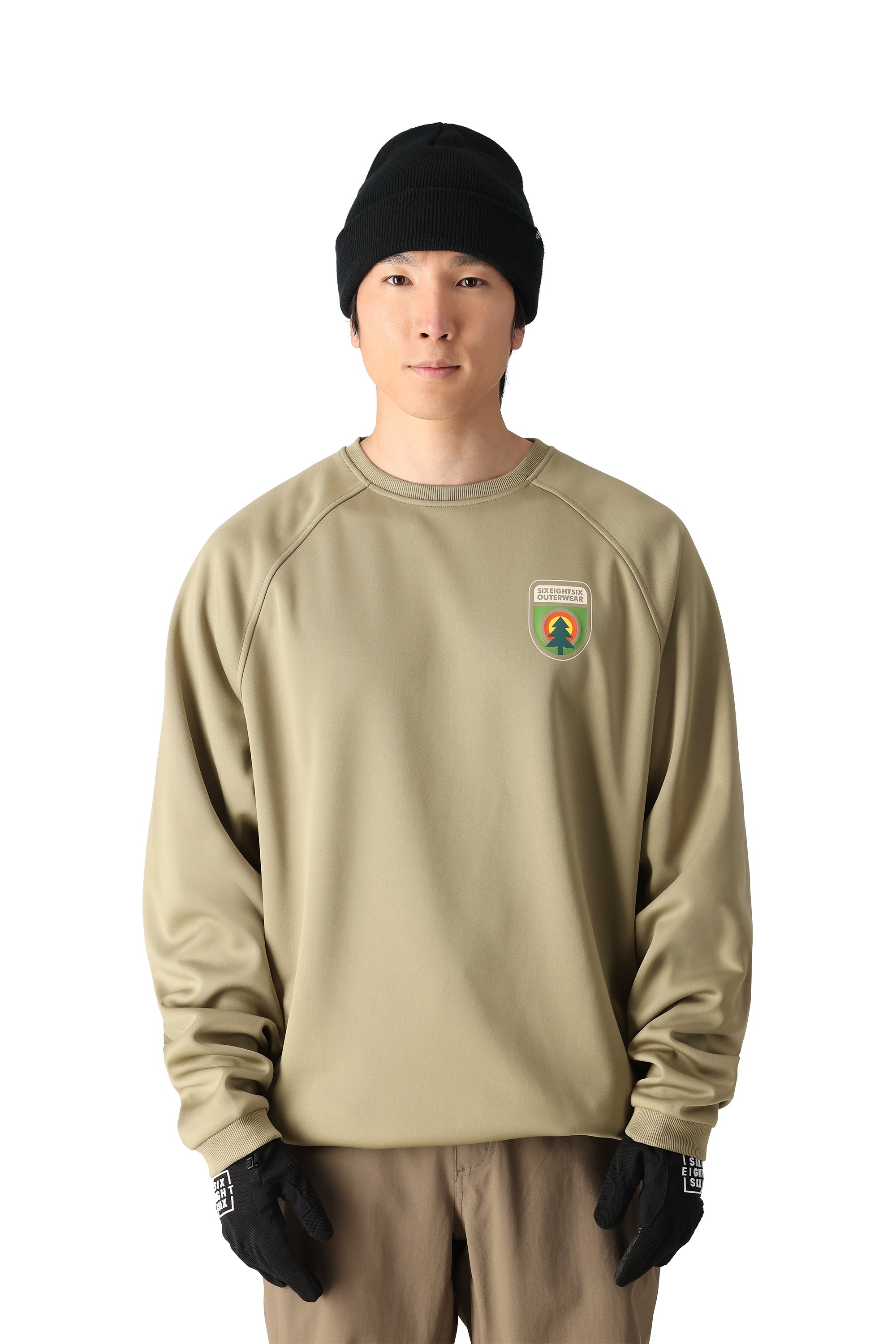 The 686 Men's Bonded Fleece Crew 2025 has a predominantly dark green color with lighter green accents and appears to be worn by someone standing in front of a snowy landscape.