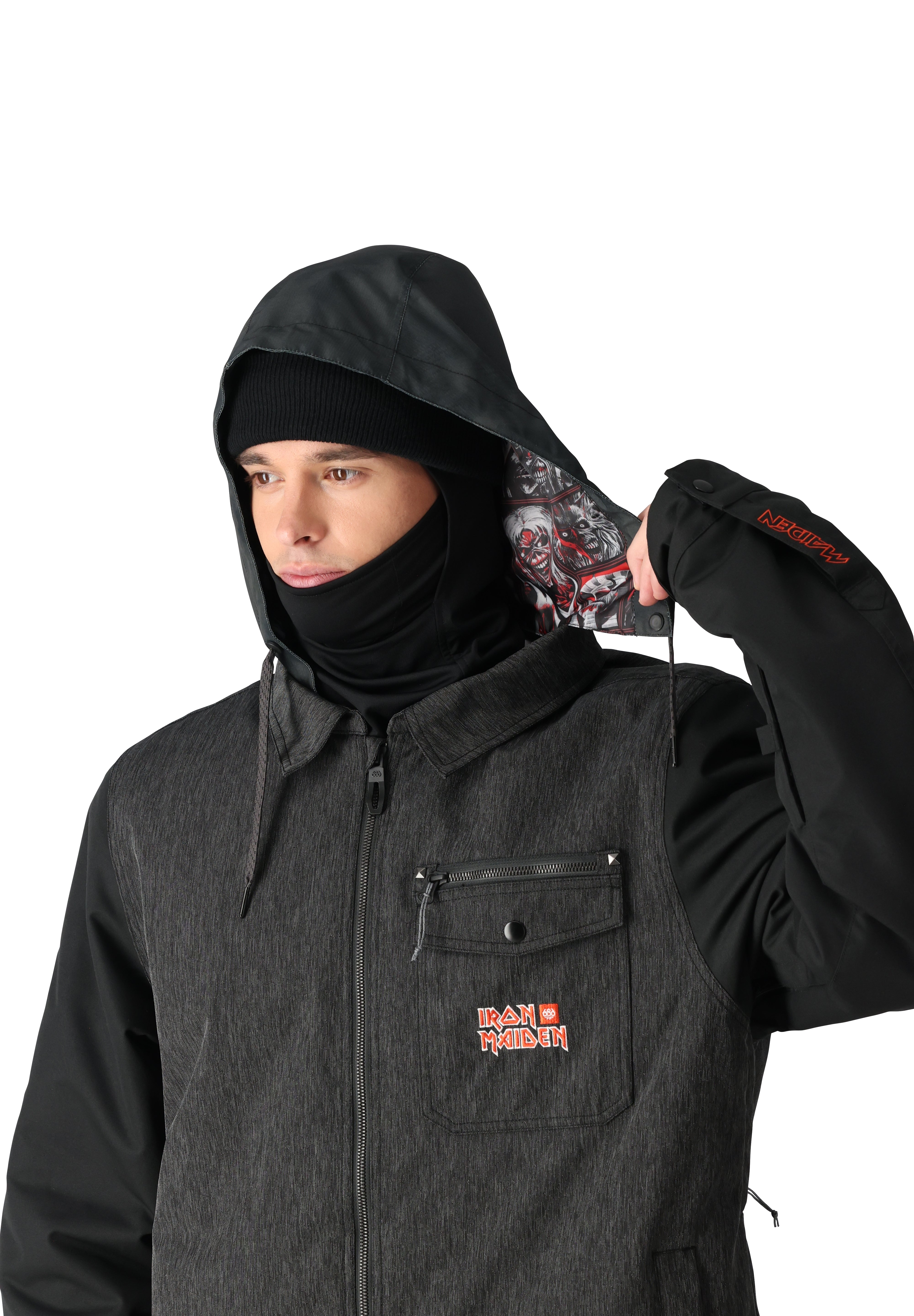 The 686 Iron Maiden Insulated Battle Jacket 2025 is dark grey with an embroidered Iron Maiden logo on the left chest and a hood featuring an illustration of Eddie from the band's album covers.