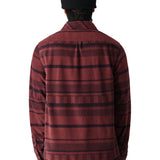 A man wearing a burgundy and black striped long-sleeved flannel shirt with a collar and button-down front stands facing away from the camera.