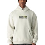 A man wearing a cream-colored 686 hoodie with two pockets and an elastic waistband.