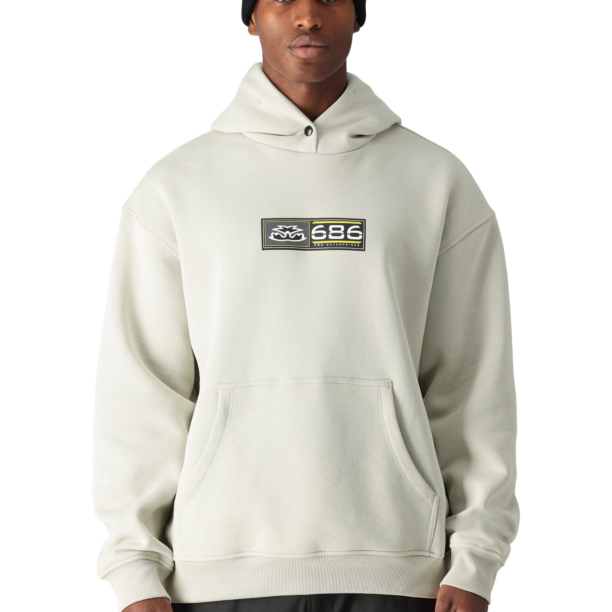 A man wearing a cream-colored 686 hoodie with two pockets and an elastic waistband.