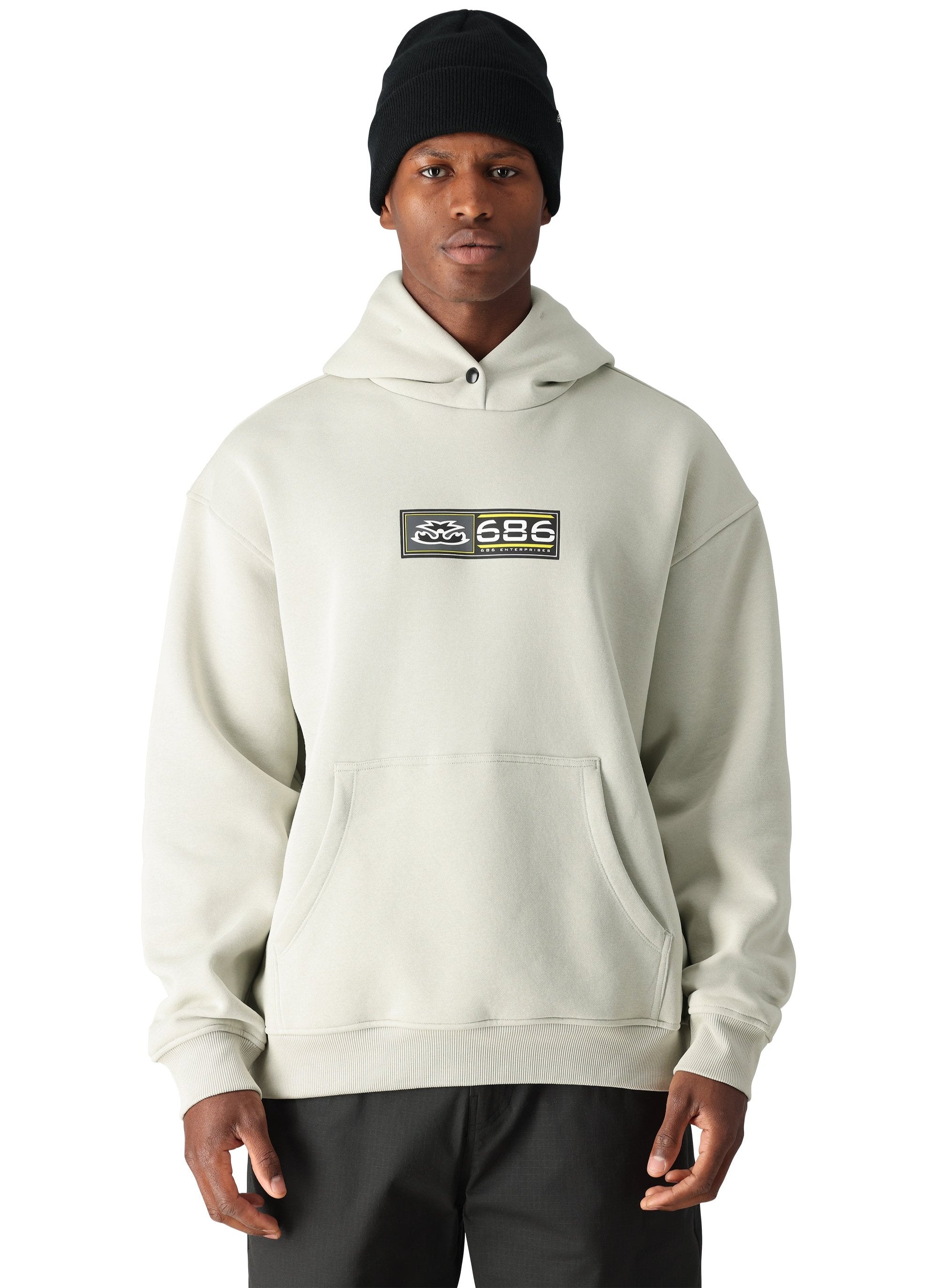 A man wearing a cream-colored 686 hoodie with two pockets and an elastic waistband.