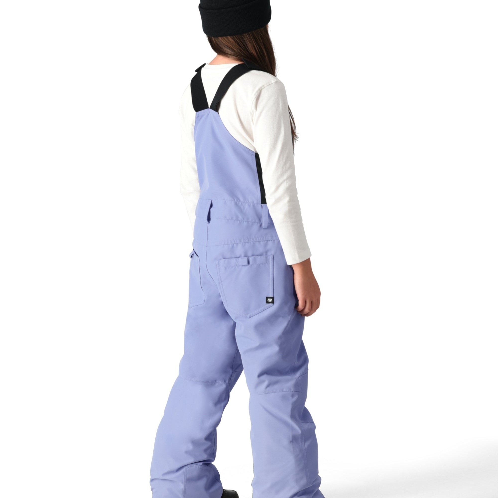 The 686 Girl's Sierra Insulated Bib Pant, shown from the back, is light blue with black suspenders and a white tag on the right side seam.