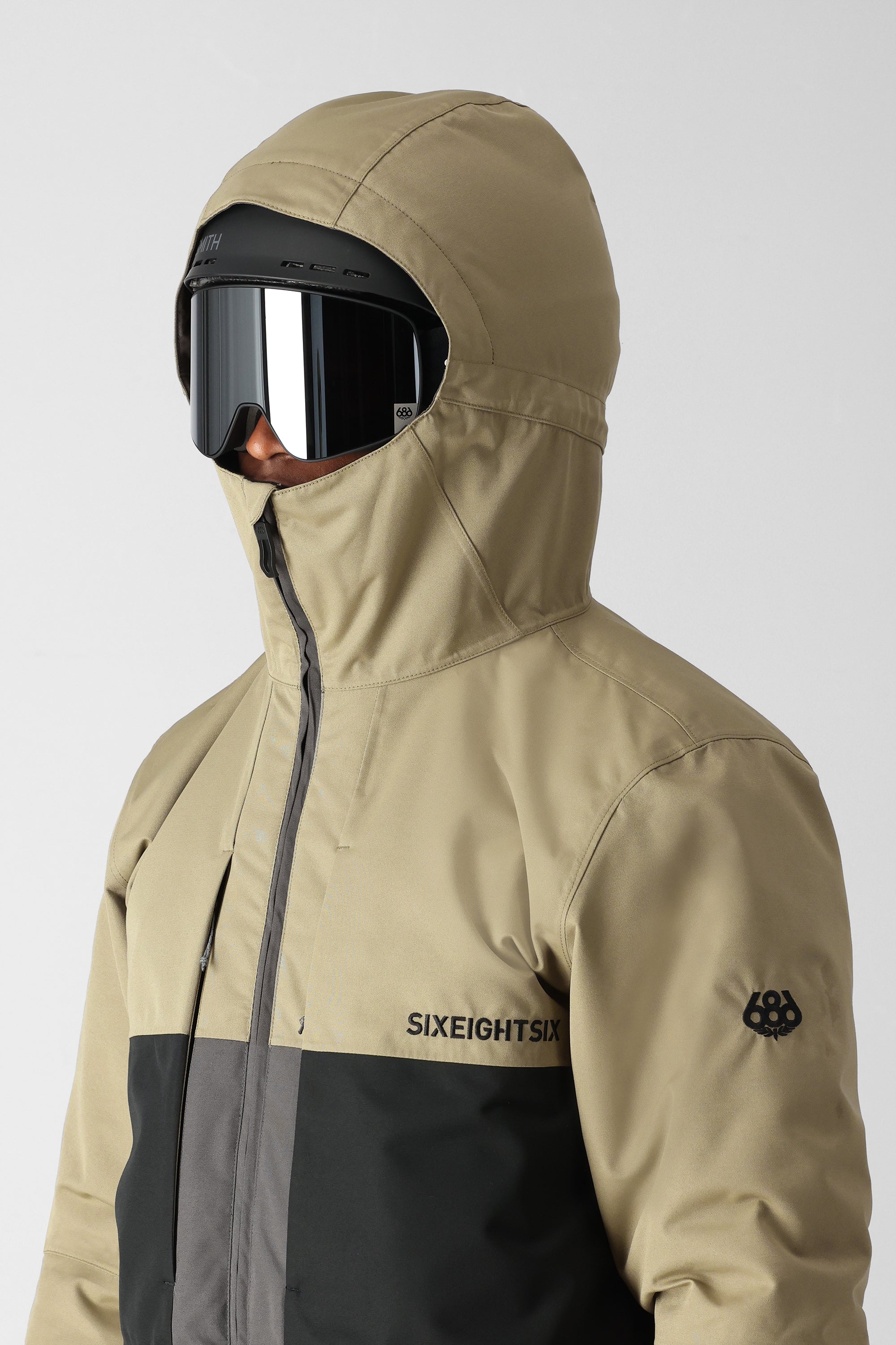 The 686 Smarty 3-in-1 Form Jacket is primarily tan with black accents and has an insulated hood.