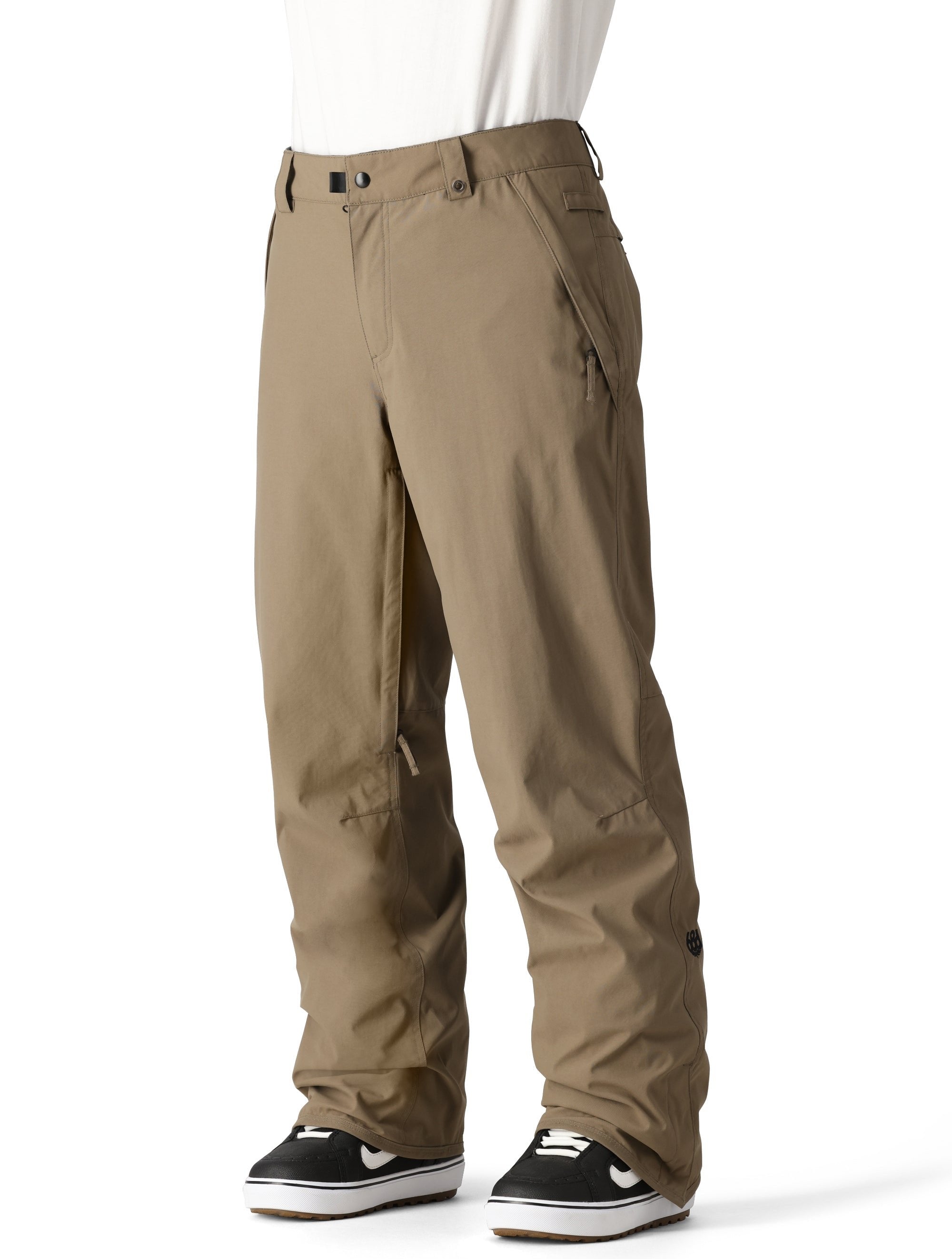 The 686 brand Men's Standard Shell Pant 2025 has a khaki color with multiple zippered pockets on both sides and an adjustable waistband.