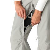 The 686 Women's Standard Shell Pant 2025 is primarily light gray with a black mesh lining visible through the split at the seam on the left leg.