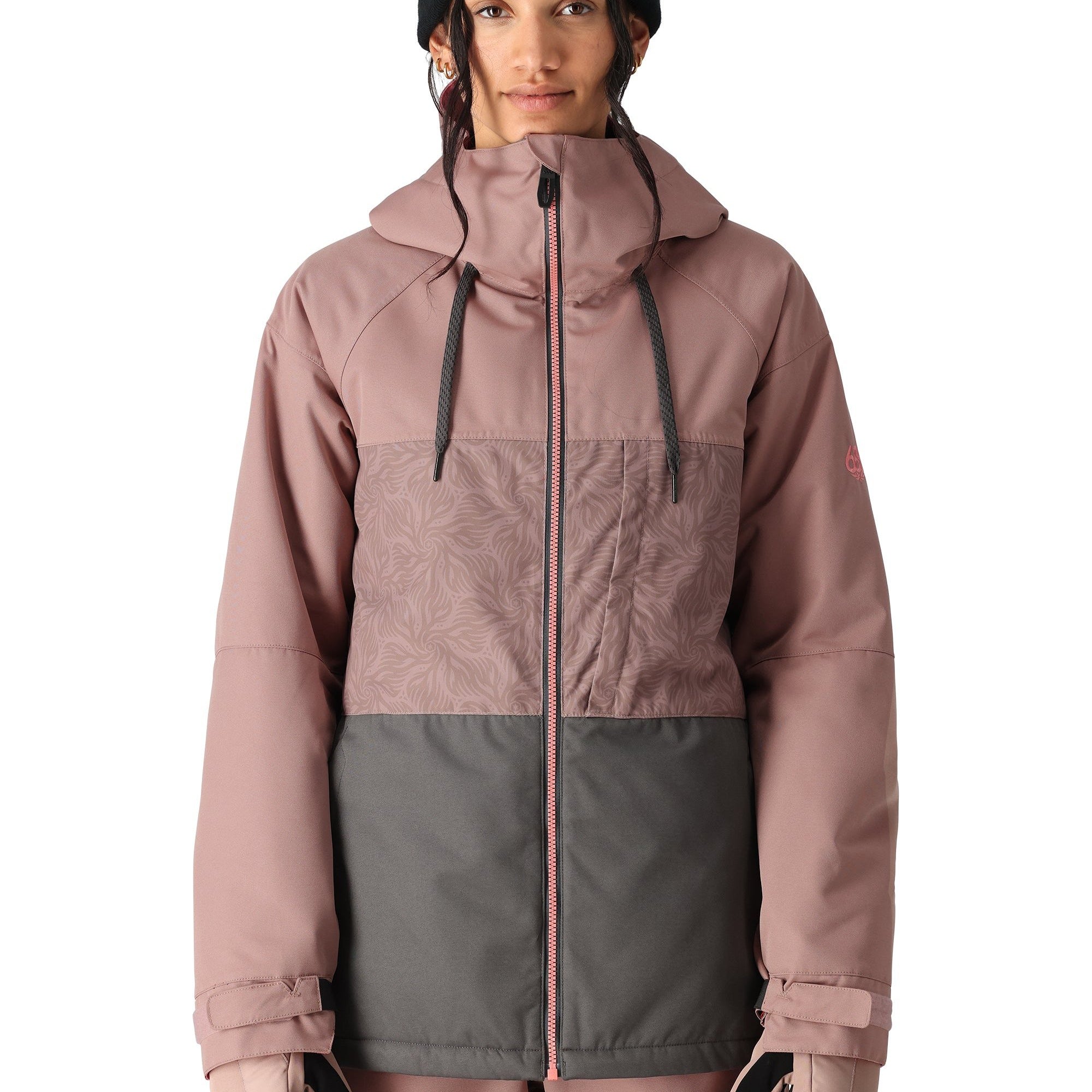 The 686 Athena Insulated Jacket in dusty rose and grey has a patterned chest section, black drawstrings on the hood, and a pink zipper down the front.