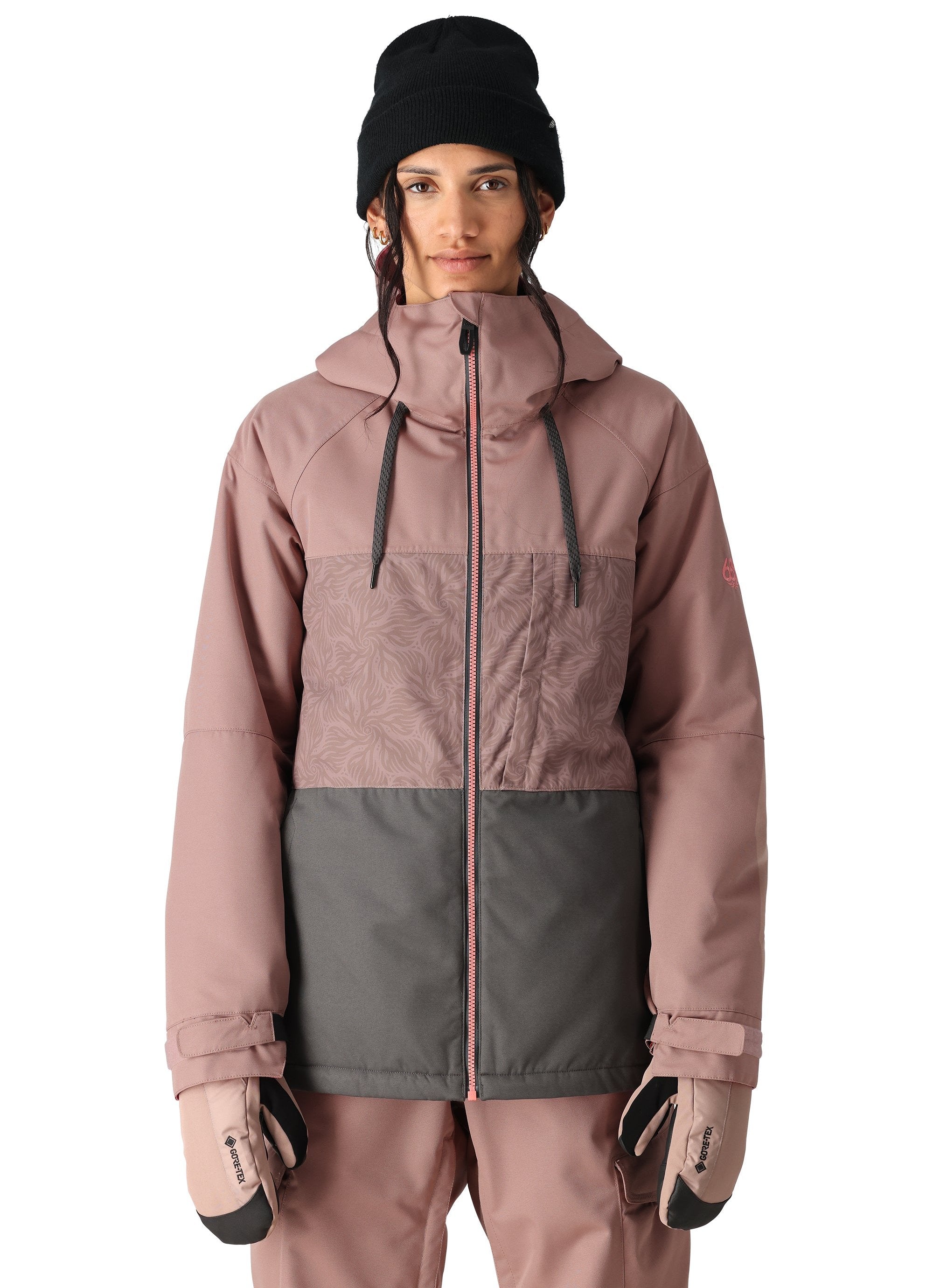 The 686 Athena Insulated Jacket in dusty rose and grey has a patterned chest section, black drawstrings on the hood, and a pink zipper down the front.