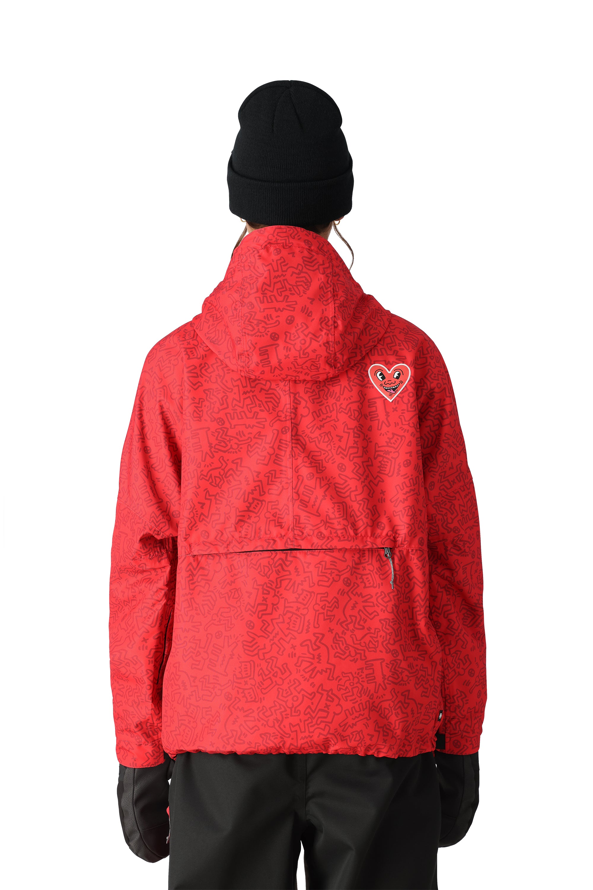 The 686 Women's Outline Shell Anorak 2025 is showcased in this image, wearing a vibrant red jacket with black accents and a heart-shaped logo on the left sleeve.