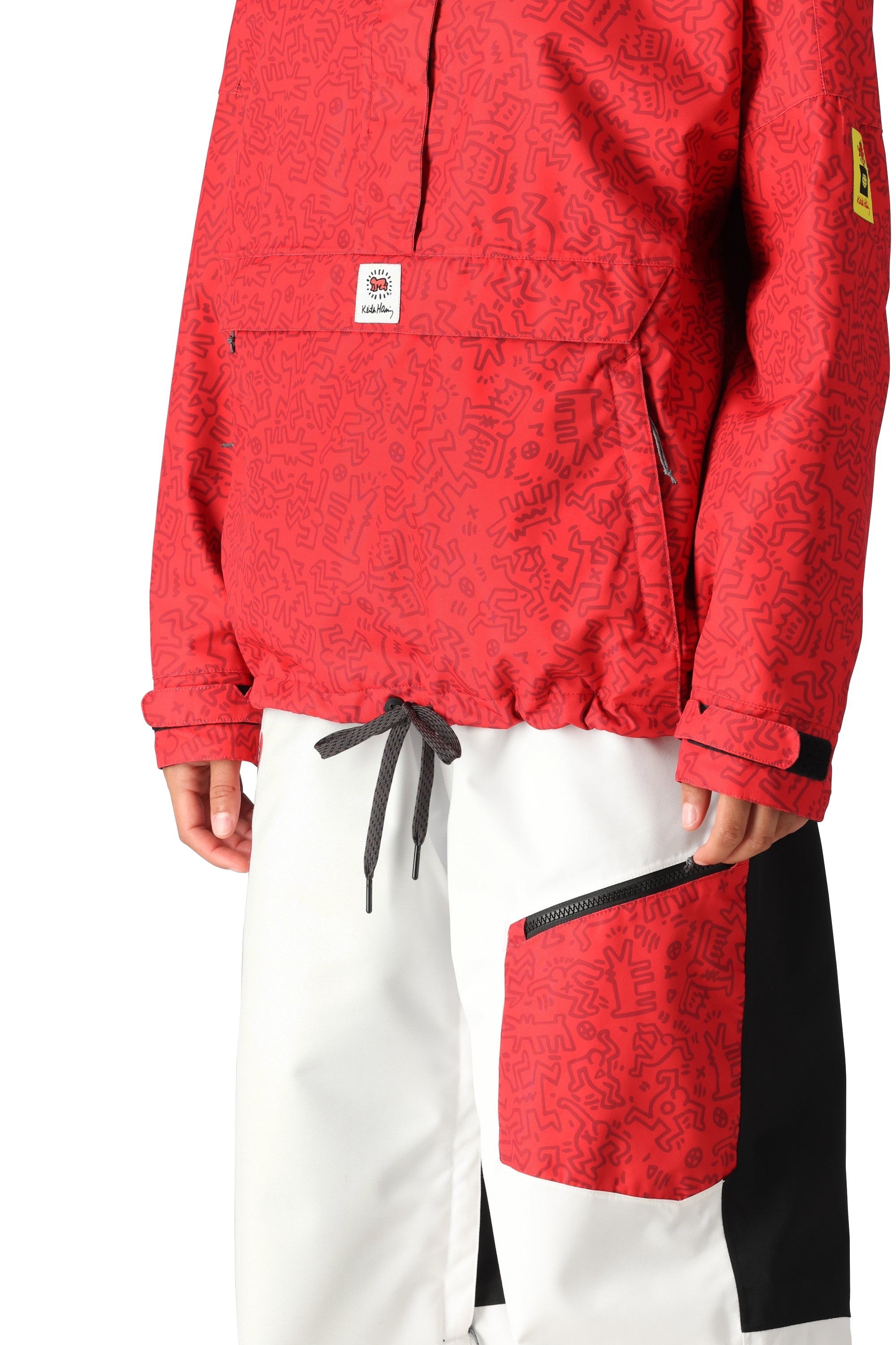 The 686 Women's Outline Shell Anorak 2025 is primarily red with a black pattern and has an adjustable drawcord at the waist.