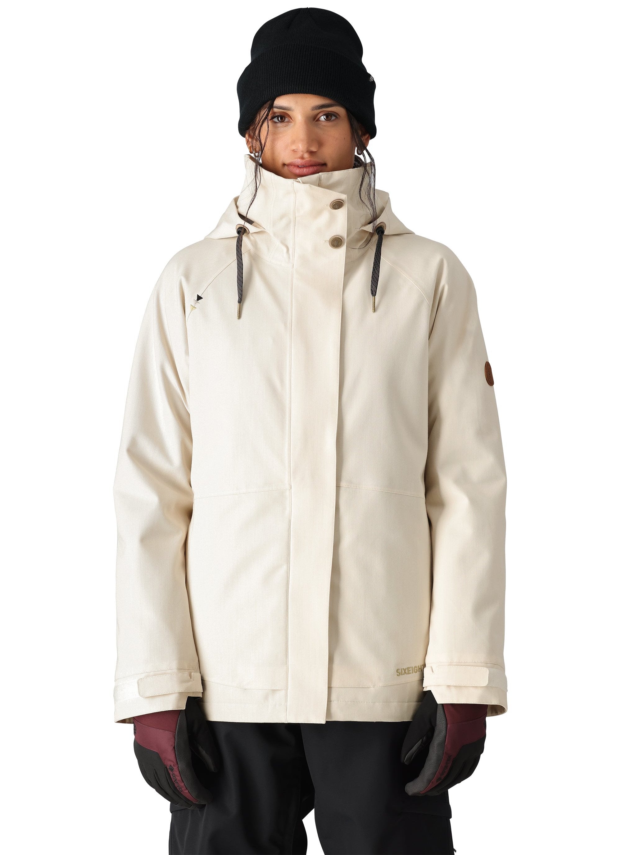 The 686 Women's SMARTY 3-in-1 Spellbound Jacket features a cream-colored design with a high collar and zippered pockets on both sides, as seen from the front view.