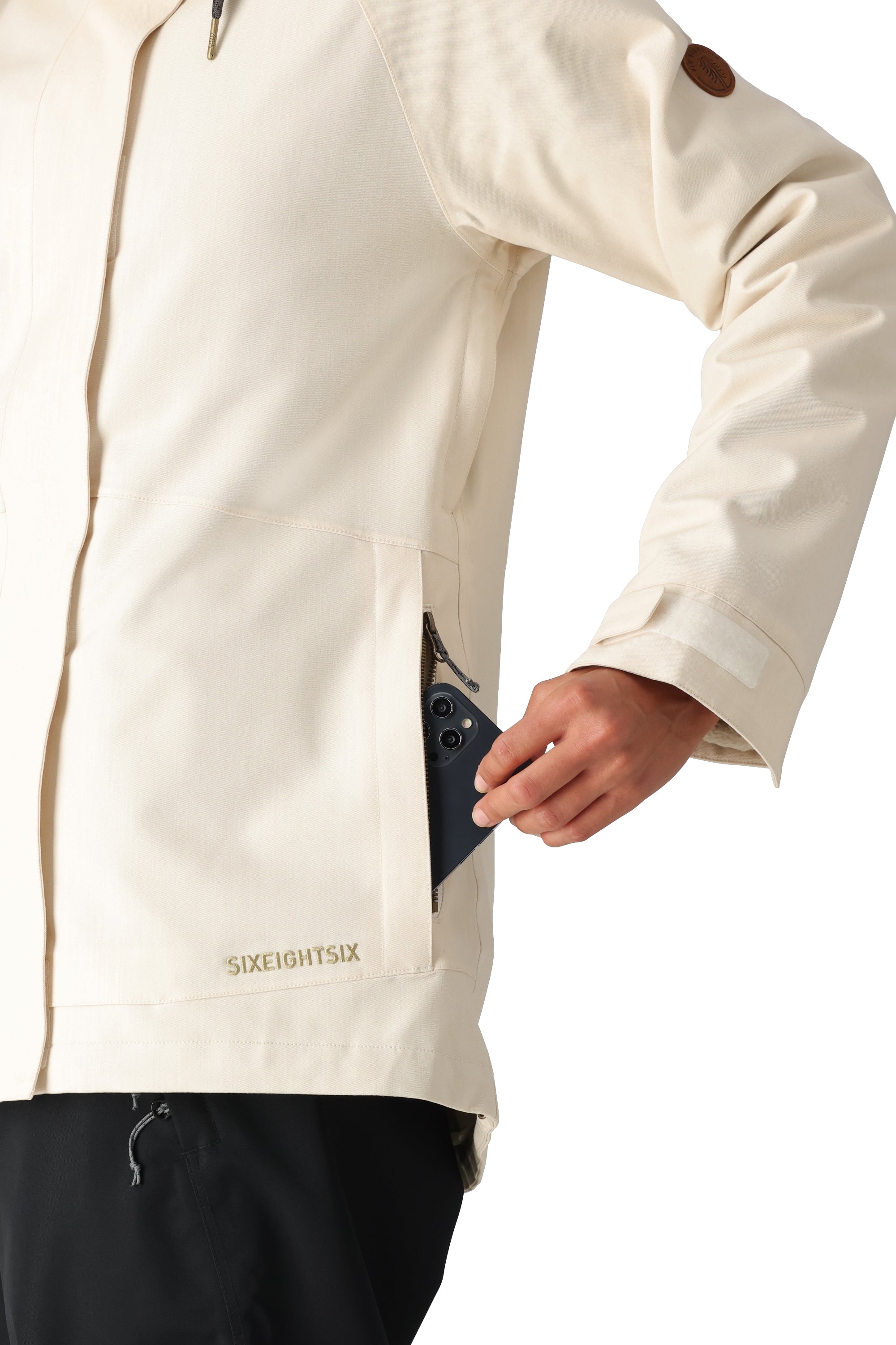 The 686 Women's SMARTY 3-in-1 Spellbound Jacket in cream features a front zip closure and two zippered pockets on the side.