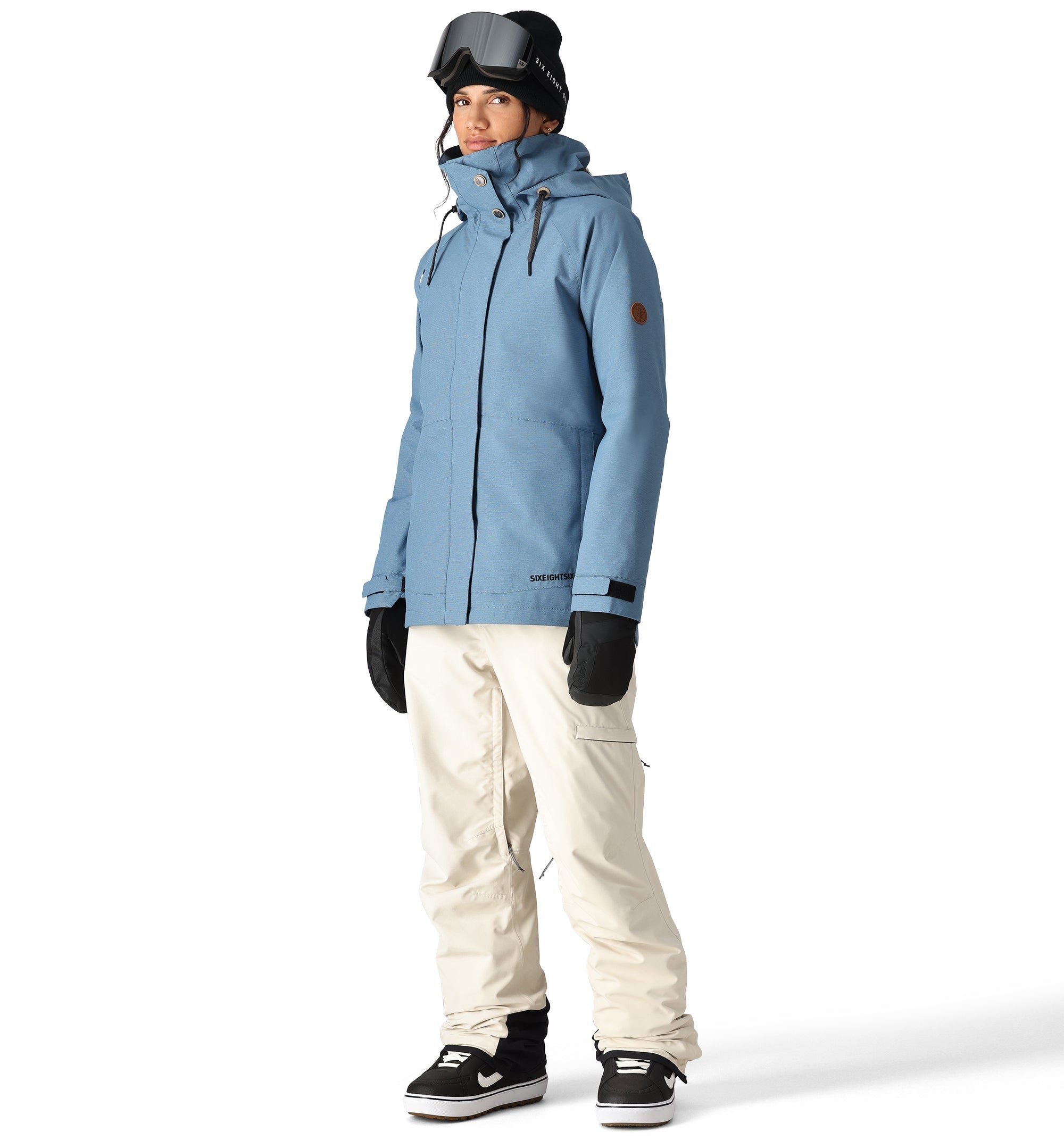 The 686 Women's SMARTY 2025 Spellbound jacket is light blue with a brown patch on one sleeve and a hood.