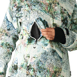The 686 Whisper Insulated Jacket for women has a white base with a black leaf pattern and is being zipped up by a woman.