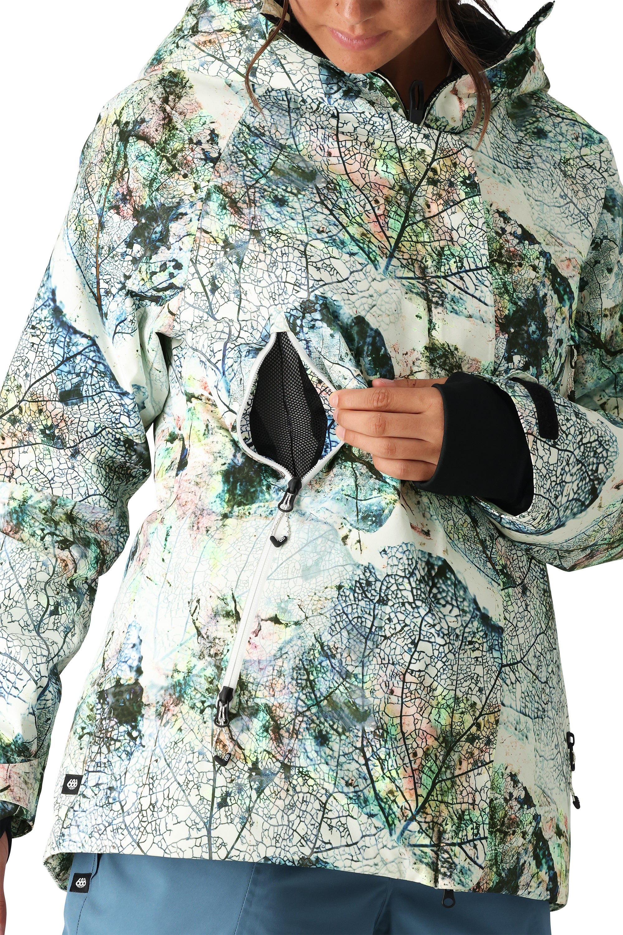 The 686 Whisper Insulated Jacket for women has a white base with a black leaf pattern and is being zipped up by a woman.