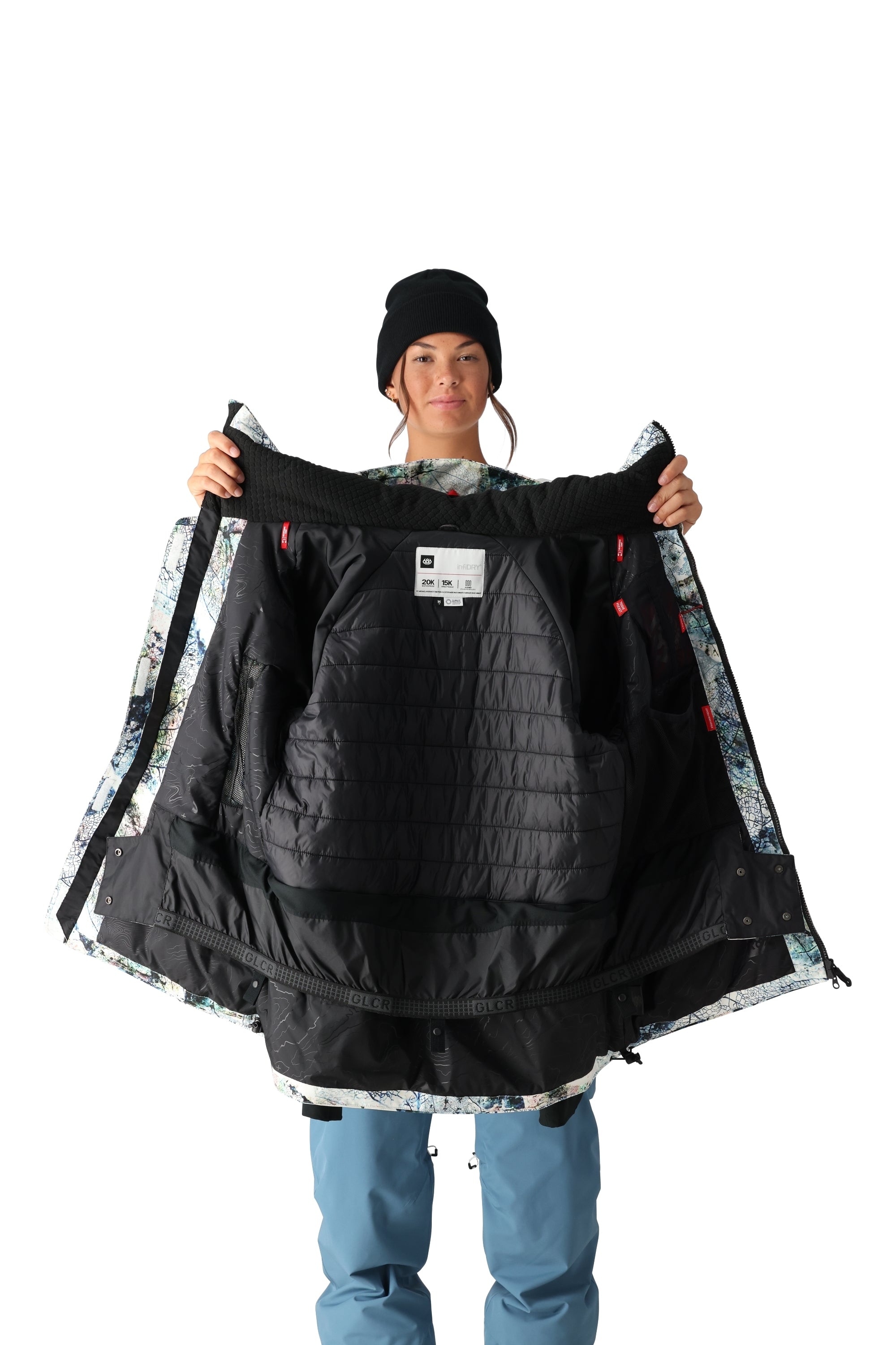 A black and white 686 snowboarding jacket with a colorful patterned lining is being held up by a woman wearing a matching beanie.