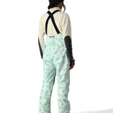 The 686 Harper Shell Bib pants are light green with a pattern of gray and pink ski trails on them.