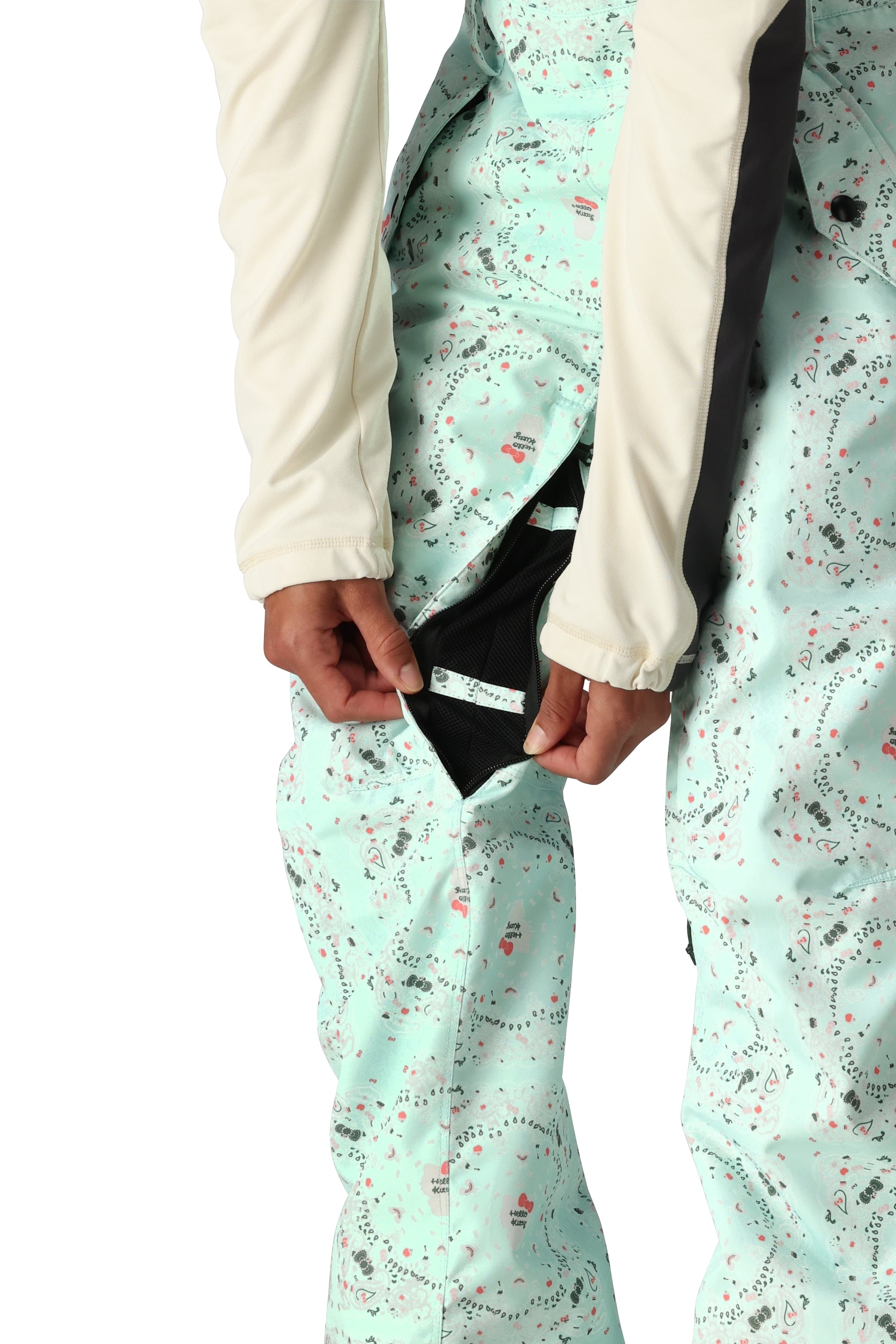 The 686 Harper bib pants have a light blue-green color with a pattern of small pink and gray shapes, and are being modeled in the front view.