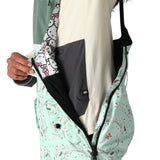 The 686 Women's Harper Shell Bib 2025 is primarily mint green with a pattern of small black and red shapes on its front view.