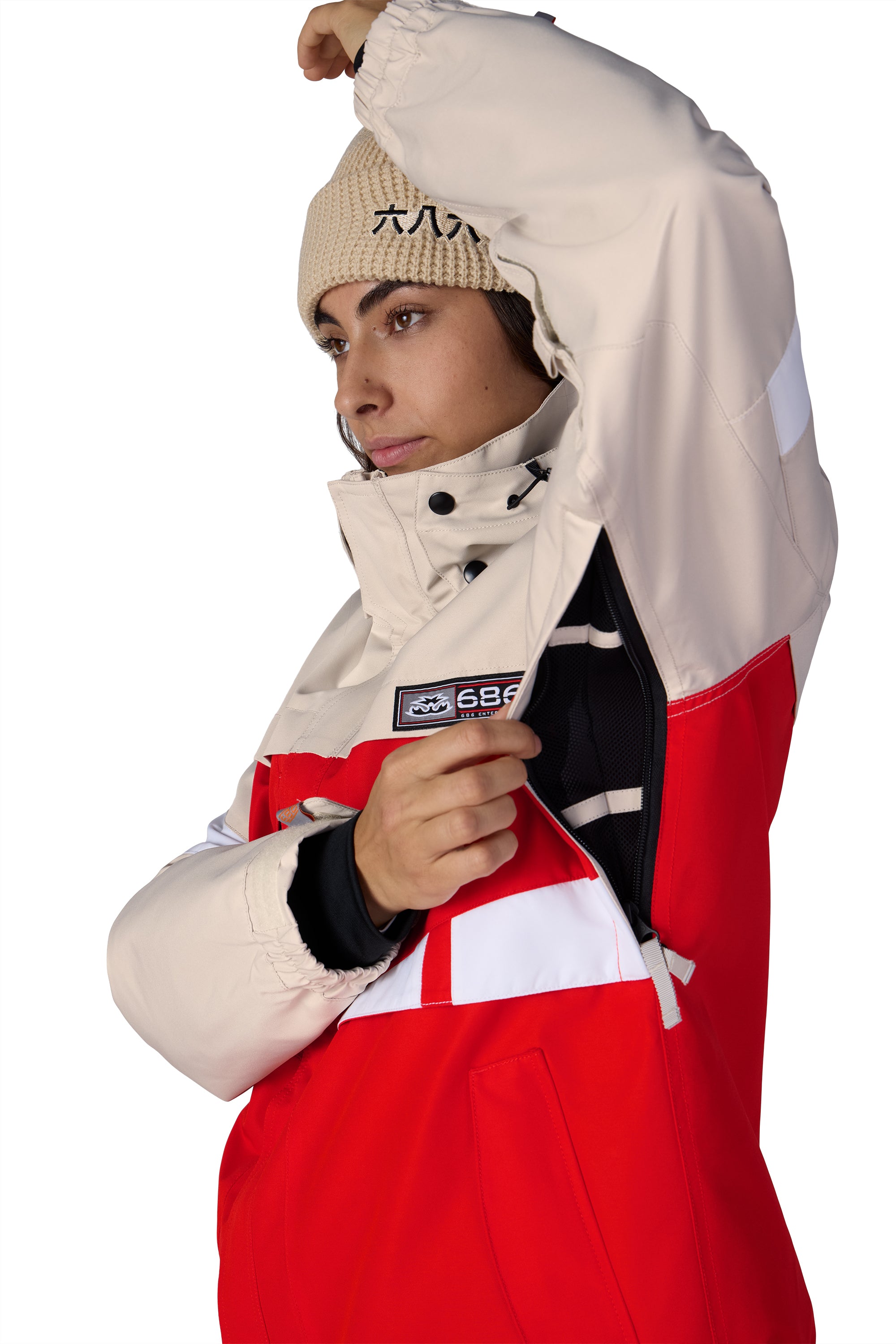 Hooded shell jacket side view; tan fabric with red lower panel and chest logo patch
