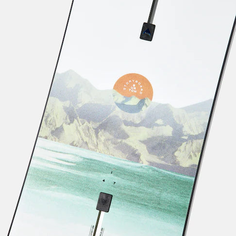 Burton Women's Family Tree Story Board B Grade Snowboard 2024 - A snowboard with a mountainous landscape and orange sun graphic on a white background.