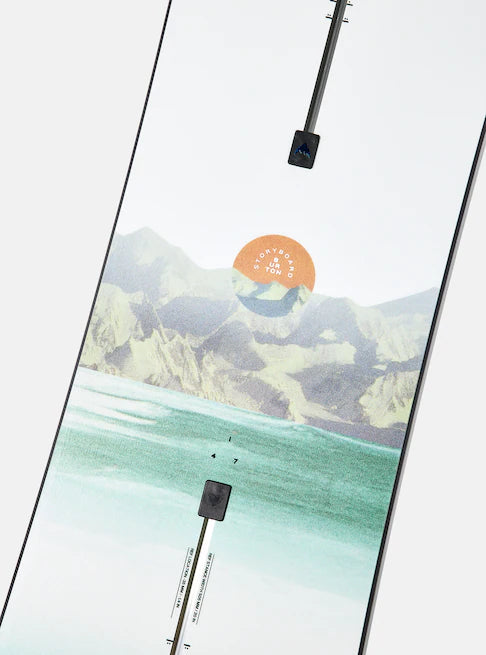 Burton Women's Family Tree Story Board B Grade Snowboard 2024 - A snowboard with a mountainous landscape and orange sun graphic on a white background.