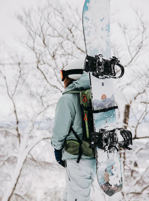 Burton Women's Family Tree Story Board B Grade Snowboard 2024 - A white snowboard with a blue and orange graphic design, featuring a mountain range and trees.