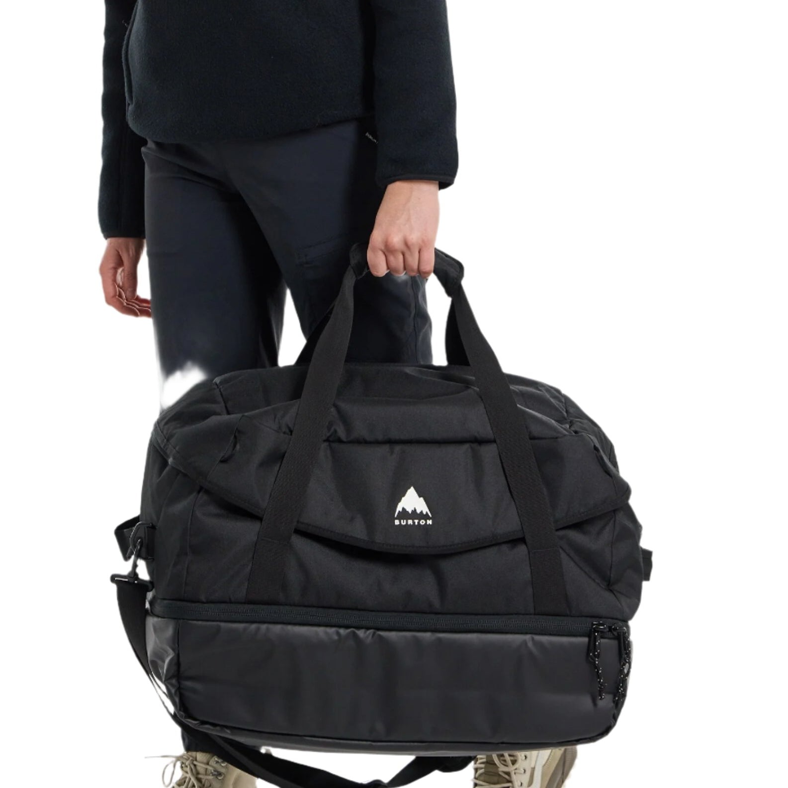 Burton Gig 70L Duffel Bag - A large black duffel bag with a white logo featuring a mountain peak and the word "BURTON" in small letters, held by a person wearing dark pants.