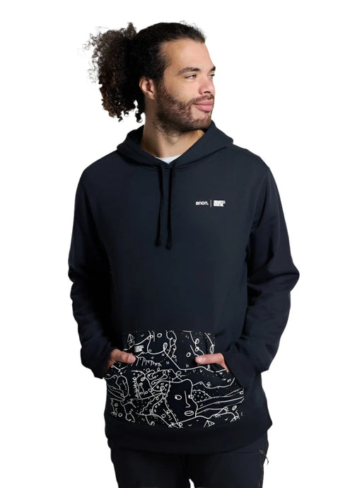 A man with curly hair tied back, wearing a black hoodie. The hoodie has a white "anon." logo and "Shantell Martin" text on the left chest, and a front pocket with a white abstract line drawing.