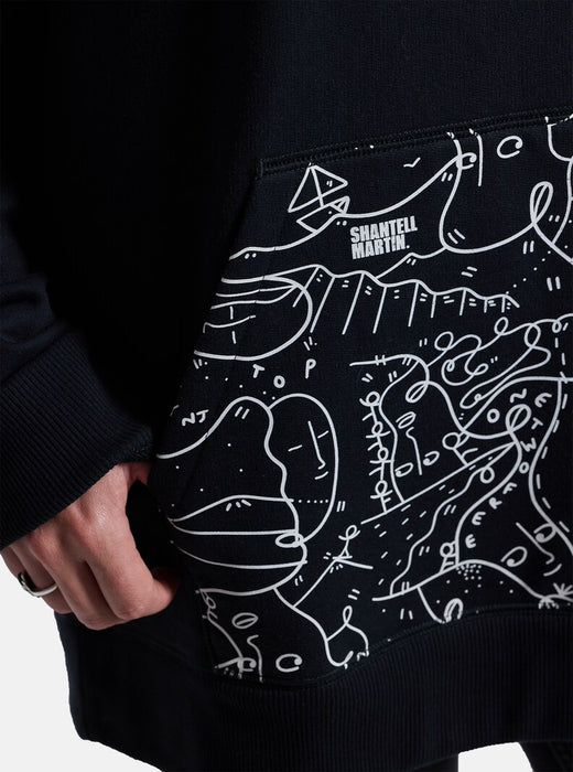 Close-up view of the front pocket on a black hoodie. The pocket features a white abstract line drawing, and the text "Shantell Martin" is visible on the upper left corner of the pocket.