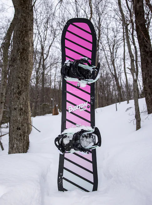 Burton Junior's Smalls Snowboard 2025 - A pink snowboard with black stripes and a black border, standing upright in the snow.