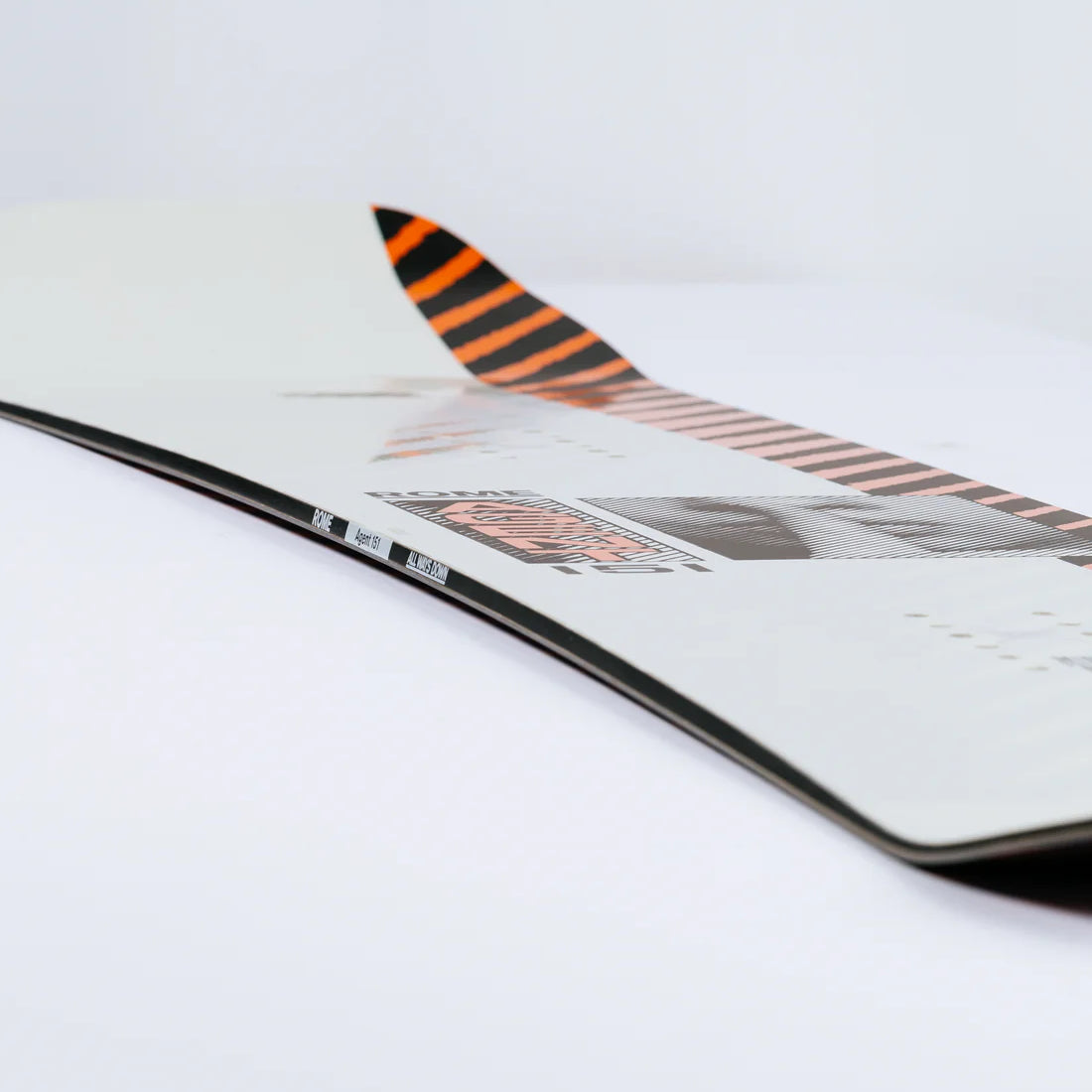 Rome Agent Snowboard 2025 - White snowboard with black and orange stripes on top of tail.